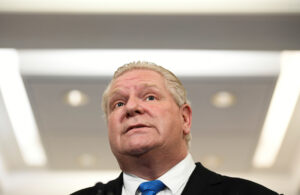 Doug Ford looking up, he is visible from the shoulders up and has white lights behind him