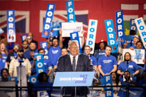 Doug Ford stands at a podium at an election rally - the crowd behind him holds FORD signs