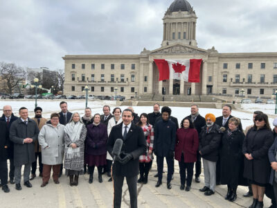 Premier Wab Kinew and members of his NDP caucus outside the legislative building hold a press conference in Winnipeg on Tuesday Mar. 4, 2025. Premier Kinew announced Tuesday that United States alcohol products are being pulled from Crown-owned Manitoba liquor stores in retaliation for tariffs imposed on Canadian goods by the U.S. government. THE CANADIAN PRESS/Steve Lambert